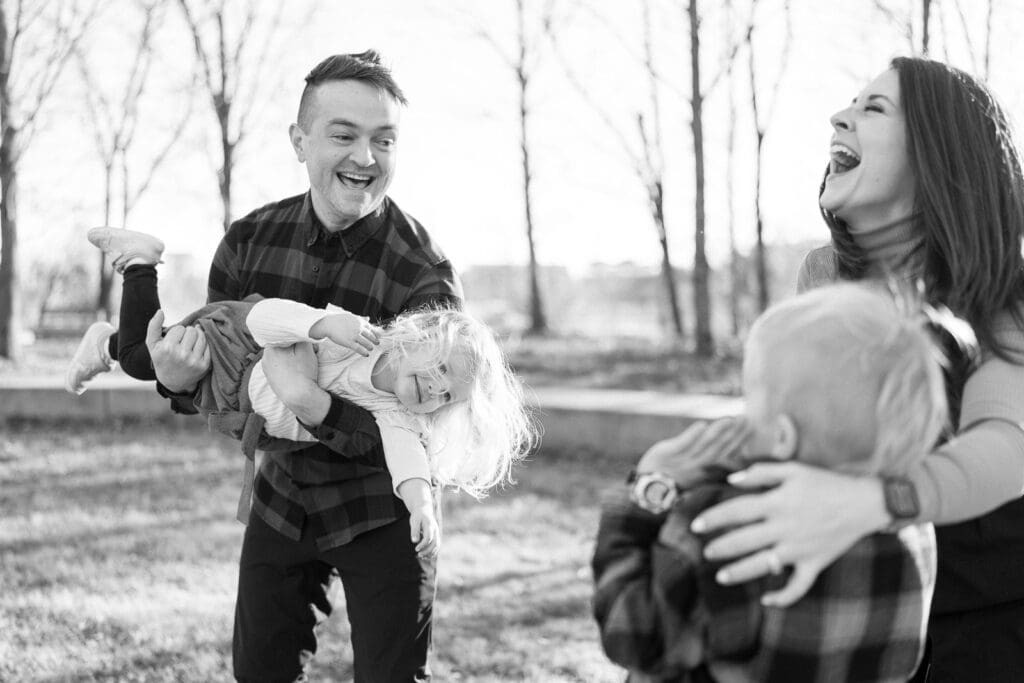 Dad playing airplane with daughter and mom and son laughing